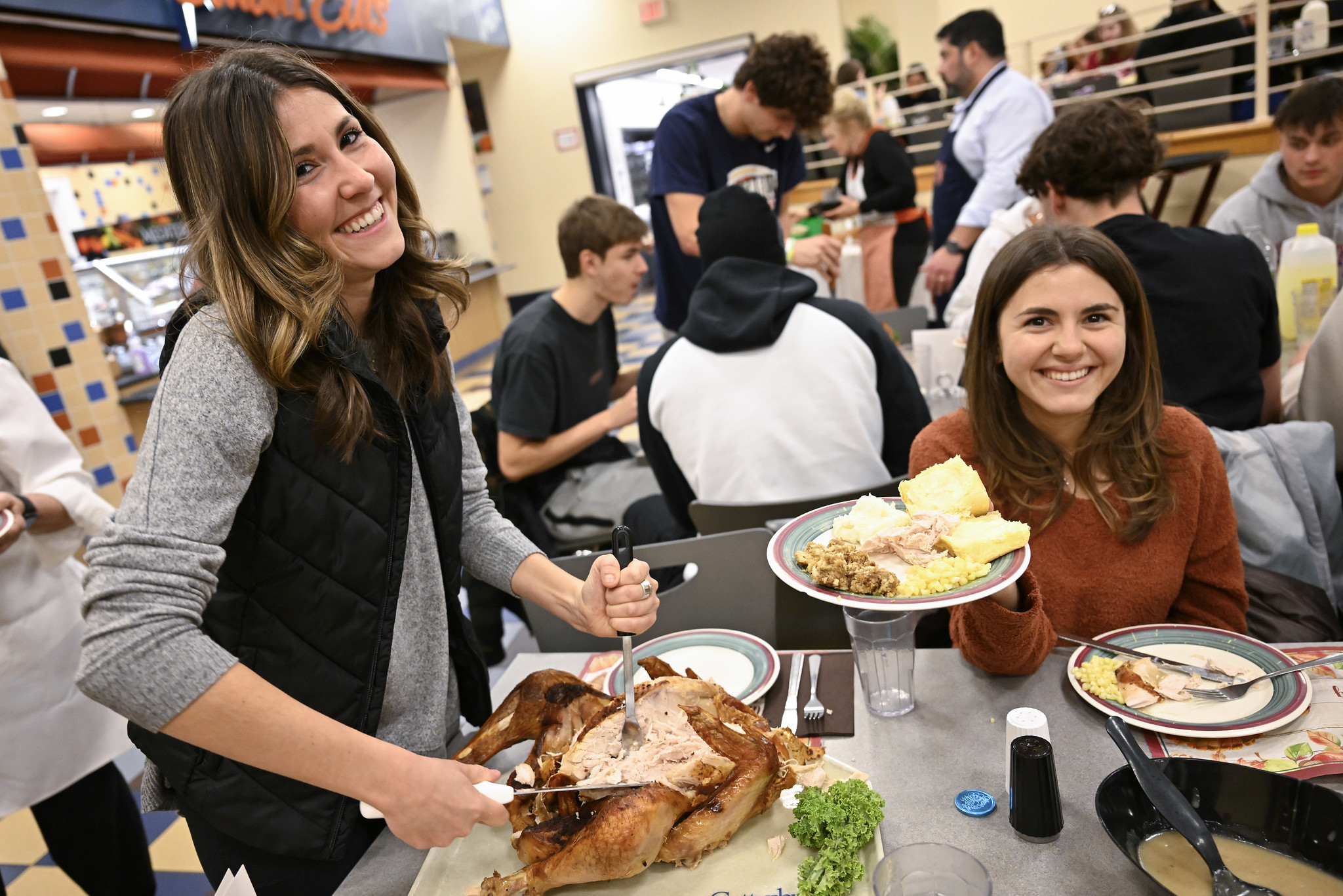 2 Students at Servo's Thankgivining dinner with a plate of food consisting of Turkey, corn, mashed potatoes and rolls